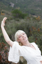 Load image into Gallery viewer, Woman in a white dress with one arm raised, standing in a natural setting.
